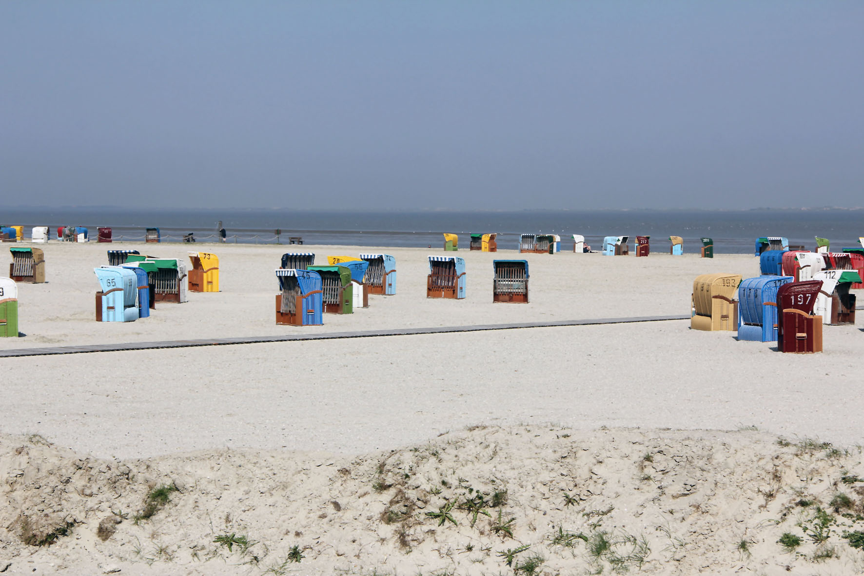 Sand, seichtes Meer und windschützende Strandkörbe im Dornumerland.
