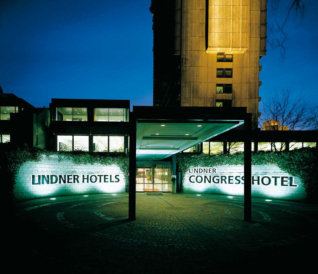 Der Eingangsbereich des Lindner Congress Hotel Düsseldorf von aussen bei Dämmerung.